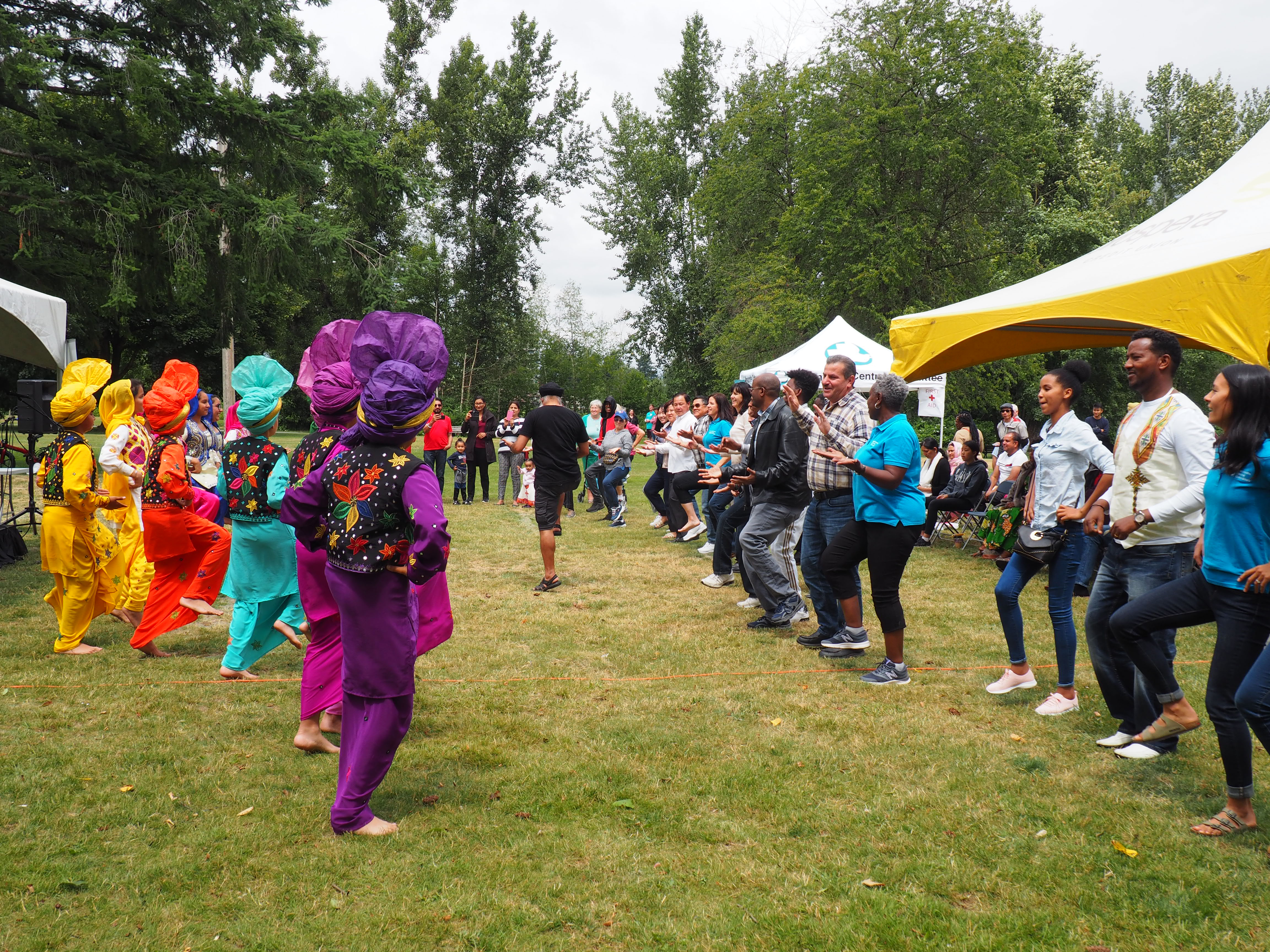 A large group of people gather in a semi circle on grass. Some are dressed in colorful traditional outfits.